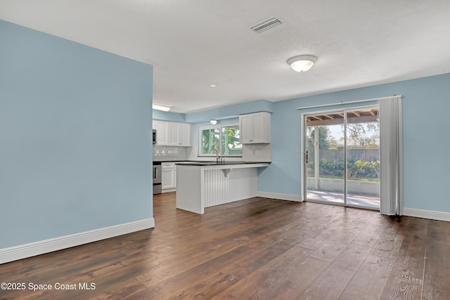 kitchen with dark wood-type flooring, backsplash, white cabinets, and a kitchen bar