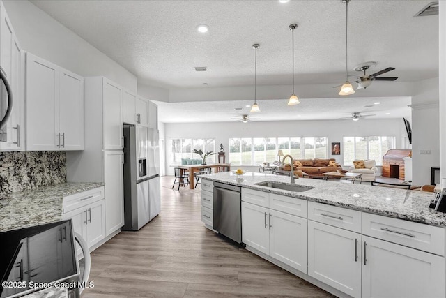 kitchen featuring appliances with stainless steel finishes, pendant lighting, white cabinetry, sink, and light wood-type flooring