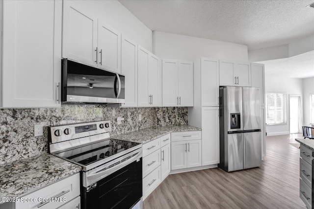 kitchen with white cabinetry, appliances with stainless steel finishes, light stone counters, and light hardwood / wood-style flooring