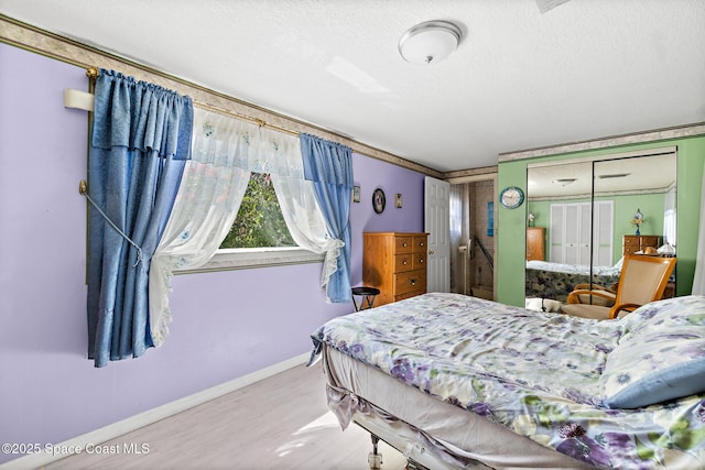 bedroom with a closet, baseboards, a textured ceiling, and wood finished floors