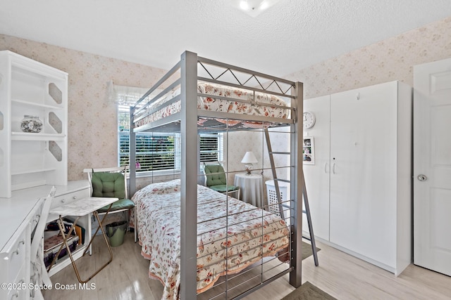 bedroom featuring a textured ceiling, wood finished floors, and wallpapered walls