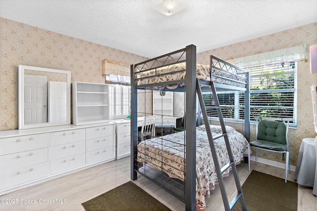 bedroom with a textured ceiling, wood finished floors, and wallpapered walls