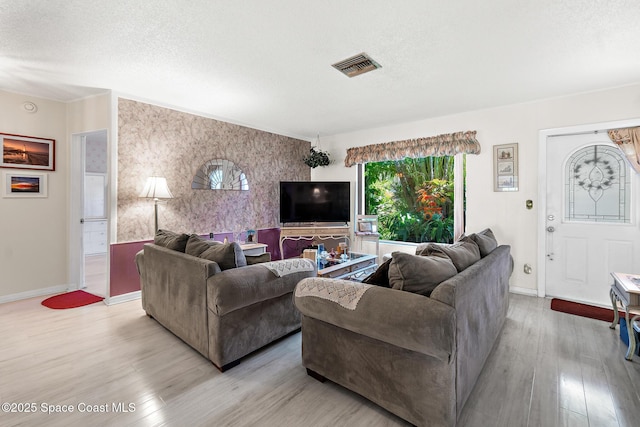 living area featuring visible vents, baseboards, a textured ceiling, and wood finished floors