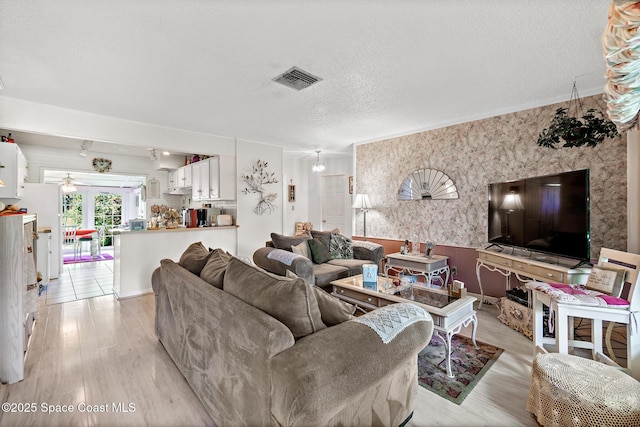 living room featuring visible vents, light wood-style flooring, and a textured ceiling