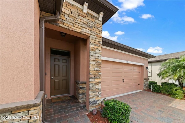 doorway to property featuring an attached garage, driveway, stucco siding, and stone siding