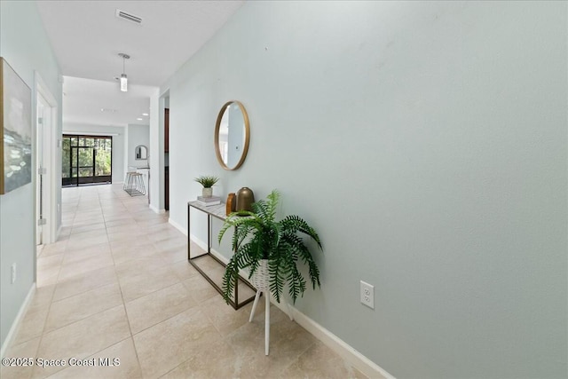 hallway with visible vents, baseboards, and light tile patterned floors