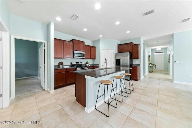 kitchen with a breakfast bar, an island with sink, visible vents, appliances with stainless steel finishes, and a sink