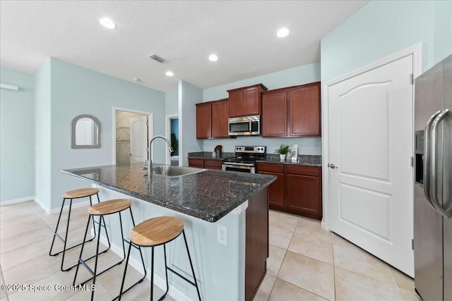 kitchen featuring a breakfast bar, a kitchen island with sink, visible vents, stainless steel appliances, and a sink