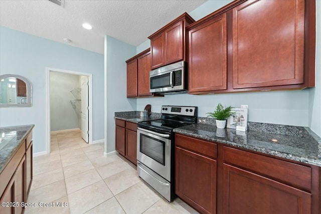 kitchen featuring dark stone countertops, light tile patterned floors, a textured ceiling, and stainless steel appliances