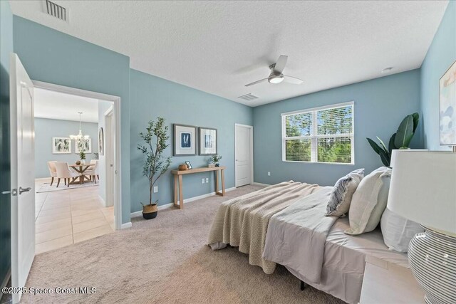 carpeted bedroom with a textured ceiling, ceiling fan with notable chandelier, visible vents, and tile patterned floors