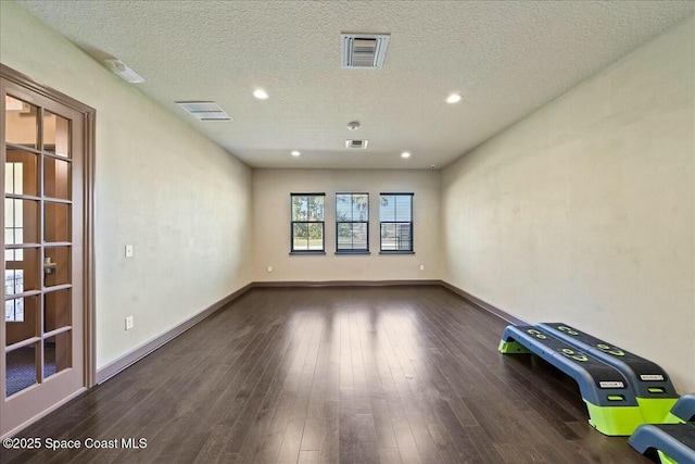 empty room with a textured ceiling, wood finished floors, baseboards, and visible vents