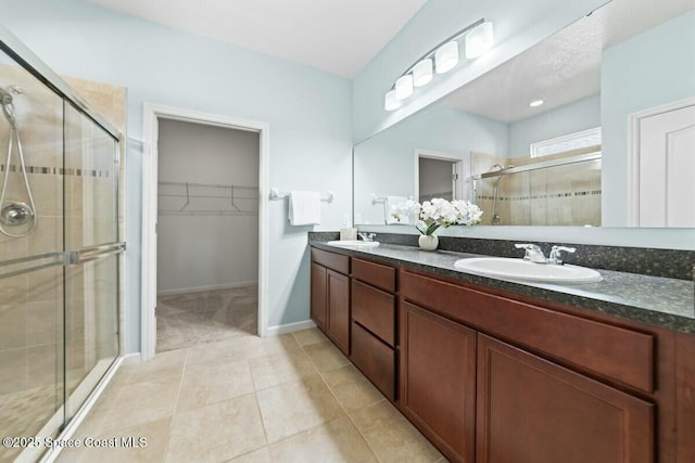 bathroom with a stall shower, a sink, a spacious closet, and tile patterned floors