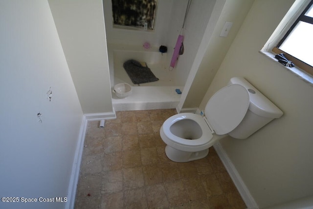 bathroom featuring a stall shower, stone finish flooring, toilet, and baseboards