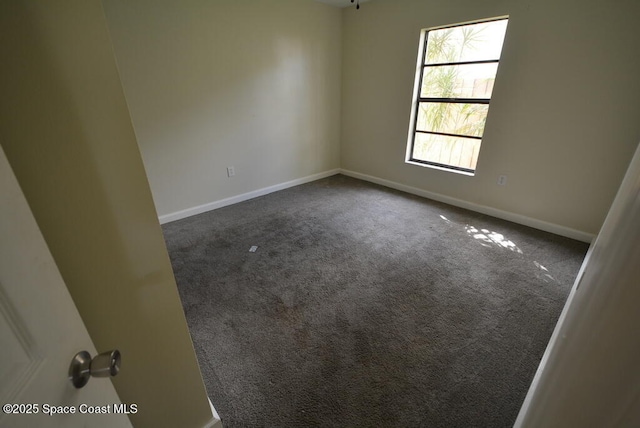 spare room with dark colored carpet and baseboards