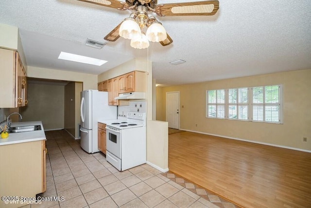 kitchen with under cabinet range hood, light countertops, light tile patterned flooring, white appliances, and a sink