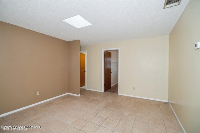 spare room with light tile patterned floors, visible vents, baseboards, and a skylight