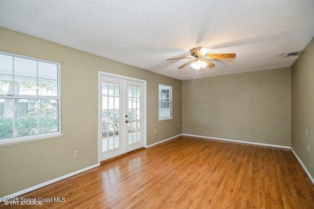 empty room featuring light wood-style flooring, baseboards, a wealth of natural light, and a textured ceiling