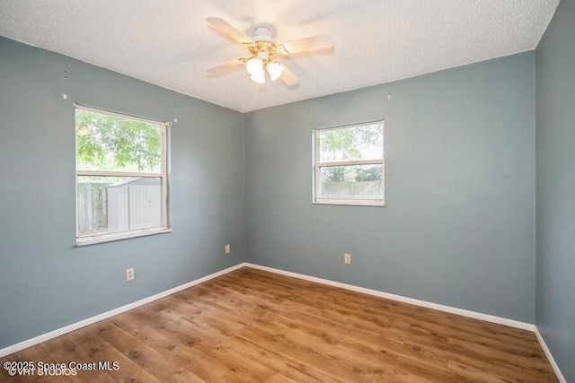 empty room featuring plenty of natural light, a textured ceiling, baseboards, and wood finished floors