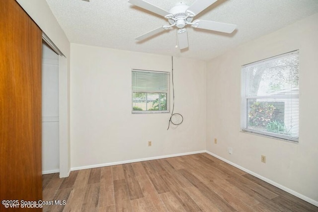 unfurnished bedroom featuring multiple windows, a textured ceiling, baseboards, and wood finished floors