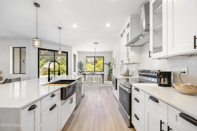 kitchen featuring pendant lighting, wall chimney range hood, sink, appliances with stainless steel finishes, and white cabinetry