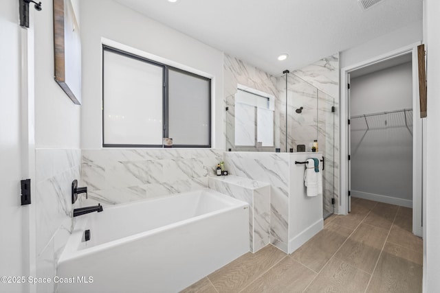 bathroom featuring a bath, tile walls, a walk in closet, recessed lighting, and a marble finish shower