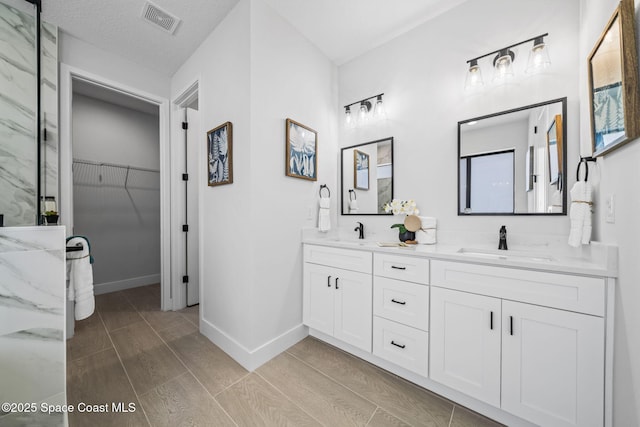 bathroom featuring a walk in closet, double vanity, visible vents, and a sink