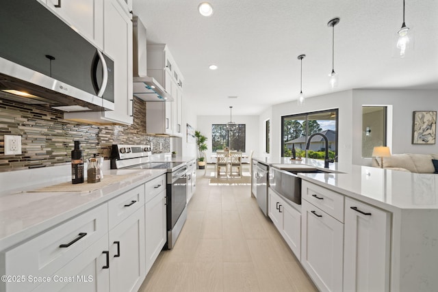 kitchen featuring wall chimney range hood, white cabinets, a sink, stainless steel appliances, and backsplash