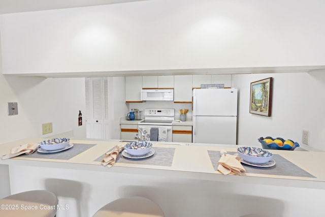 11 Plantation Dr Unit 201, Vero Beach, FL 32966 - kitchen with white appliances, a kitchen breakfast bar, kitchen peninsula, and white cabinets