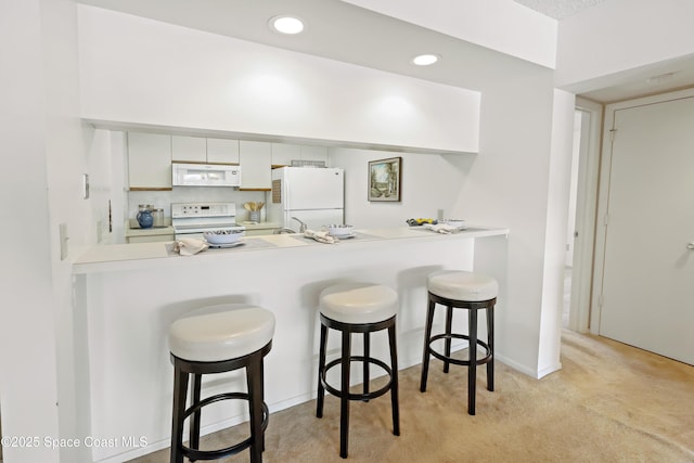 11 Plantation Dr Unit 201, Vero Beach, FL 32966 - kitchen with a breakfast bar area, white cabinets, kitchen peninsula, light carpet, and white appliances