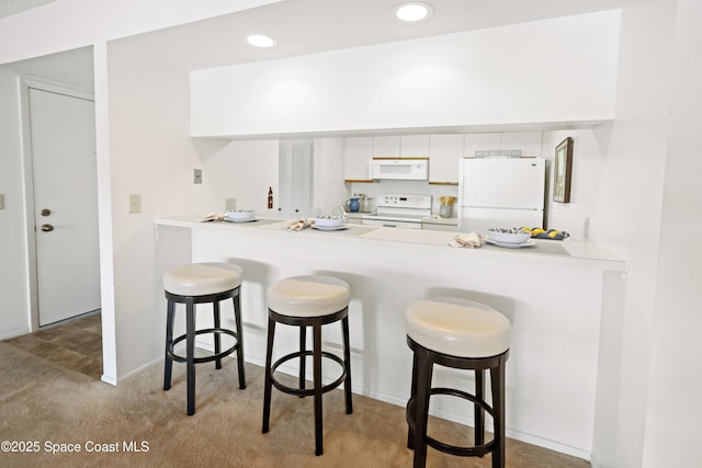 11 Plantation Dr Unit 201, Vero Beach, FL 32966 - kitchen with white cabinetry, white appliances, a breakfast bar area, and kitchen peninsula