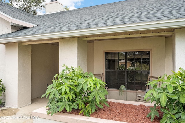 entrance to property featuring a shingled roof, a chimney, and stucco siding