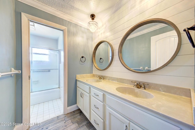 bathroom with hardwood / wood-style flooring, shower / bath combination with glass door, vanity, ornamental molding, and a textured ceiling