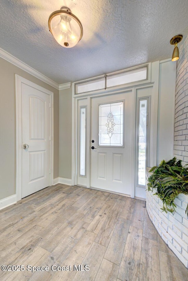 entrance foyer with ornamental molding, light hardwood / wood-style flooring, and a textured ceiling