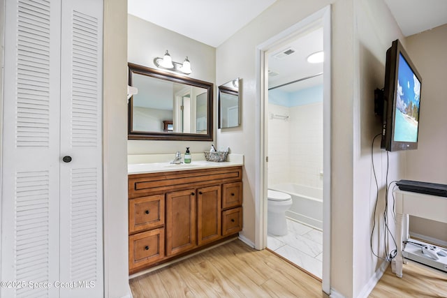 full bathroom with vanity, tiled shower / bath, wood-type flooring, and toilet