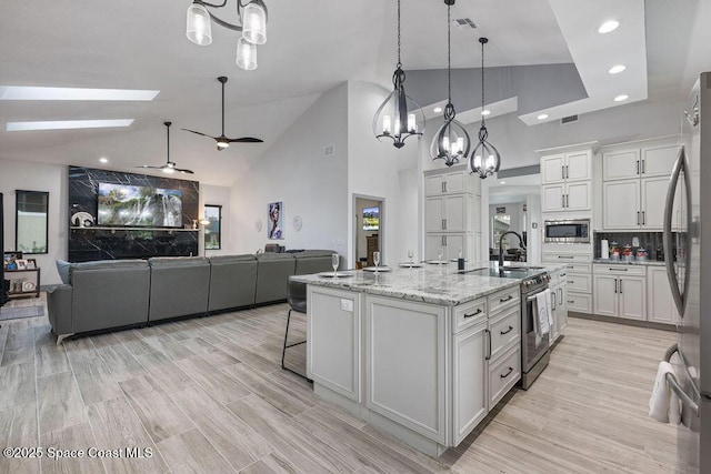 kitchen with white cabinets, an island with sink, stainless steel appliances, and hanging light fixtures