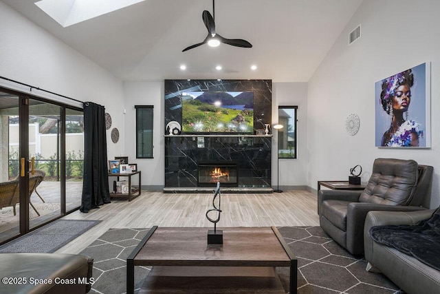 living room featuring hardwood / wood-style flooring, a skylight, ceiling fan, a premium fireplace, and high vaulted ceiling