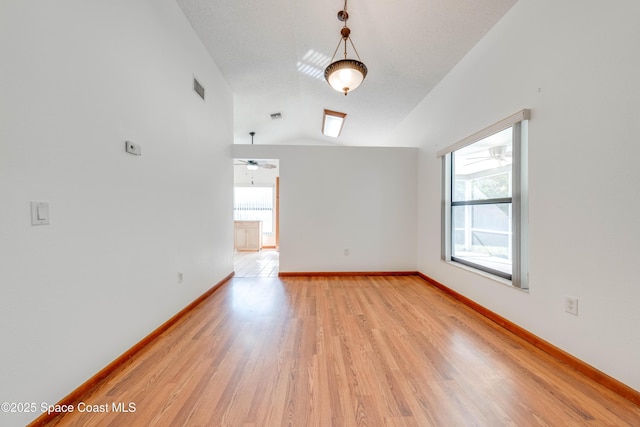 empty room with vaulted ceiling, light wood-type flooring, visible vents, and baseboards