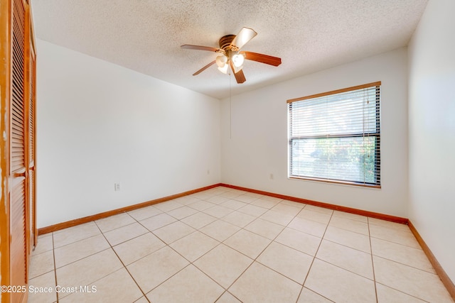 empty room with a ceiling fan, light tile patterned flooring, a textured ceiling, and baseboards