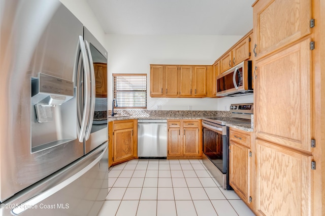 kitchen featuring stainless steel appliances, light tile patterned floors, a sink, and light stone countertops