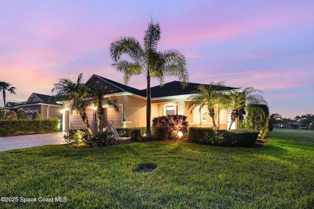 ranch-style house with a garage, a yard, decorative driveway, and stucco siding