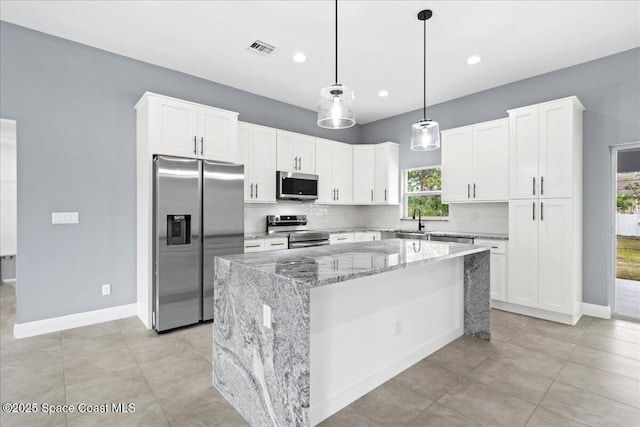 kitchen with appliances with stainless steel finishes, pendant lighting, backsplash, a center island, and light stone counters