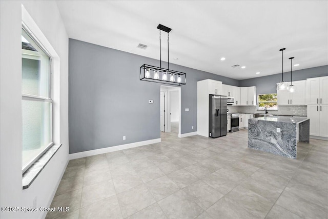 kitchen with a kitchen island, pendant lighting, white cabinetry, light stone counters, and stainless steel appliances