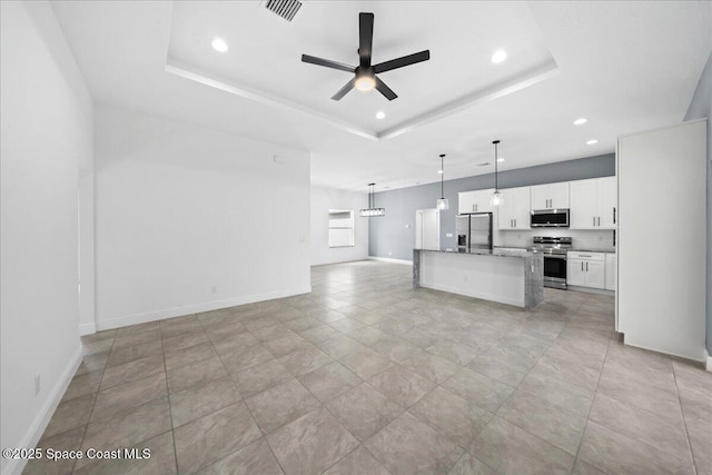 kitchen with a raised ceiling, a kitchen island, appliances with stainless steel finishes, and white cabinetry