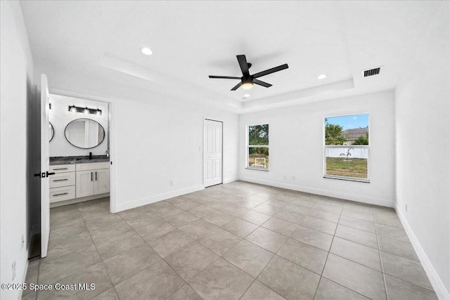 unfurnished bedroom featuring light tile patterned flooring, ensuite bathroom, sink, ceiling fan, and a raised ceiling