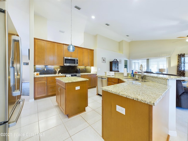 kitchen featuring sink, hanging light fixtures, stainless steel appliances, light stone countertops, and a kitchen island