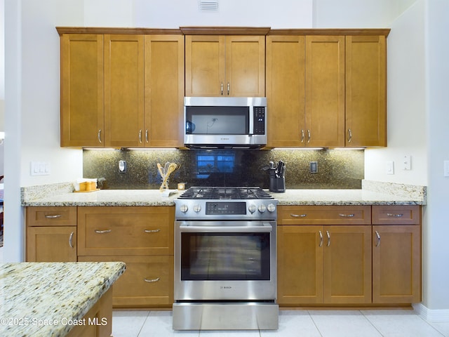 kitchen featuring light stone countertops, appliances with stainless steel finishes, light tile patterned floors, and backsplash