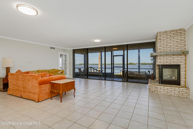 living room with a water view, light tile patterned floors, ornamental molding, a wall of windows, and a fireplace