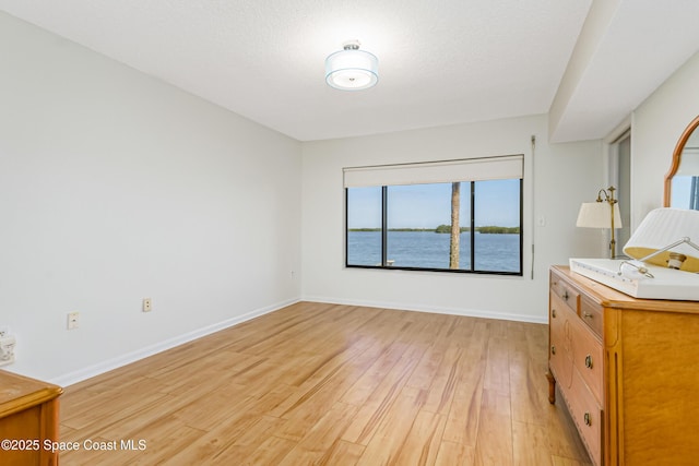 unfurnished bedroom with light wood-type flooring, a textured ceiling, and a water view