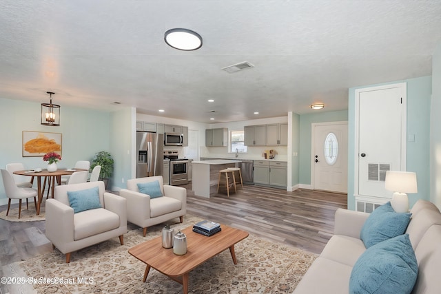 living room featuring an inviting chandelier, sink, light hardwood / wood-style flooring, and a textured ceiling