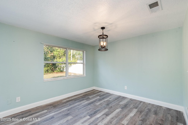 spare room with a notable chandelier, wood-type flooring, and a textured ceiling